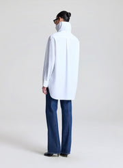 Person wearing a white collared shirt and blue jeans on a plain background