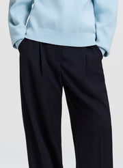 Close-up of a person wearing dark navy wide-leg trousers and a light blue ribbed sweater, cropped from the chest down against a plain light gray background.