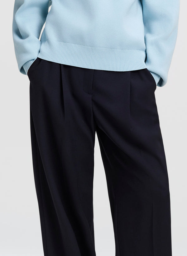 Close-up of a person wearing dark navy wide-leg trousers and a light blue ribbed sweater, cropped from the chest down against a plain light gray background.
