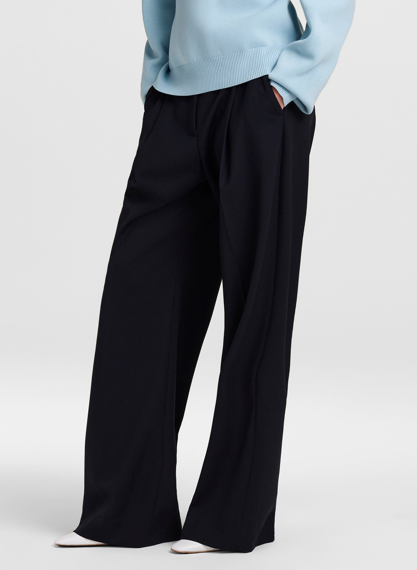 A person wearing blue wide-leg trousers with a light blue sweater, shown from the chest down against a plain light gray studio background.