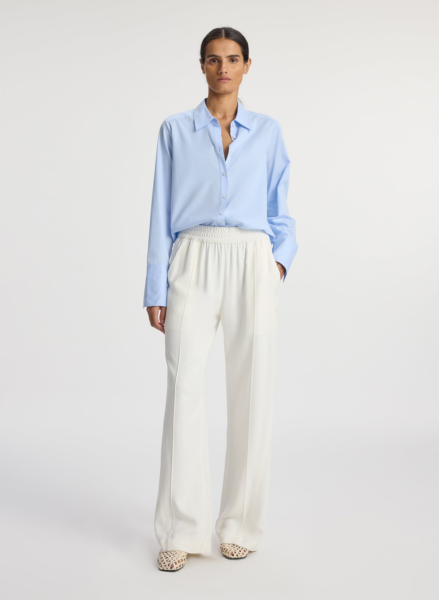 front view of woman wearing light blue button down collared shirt and white pants
