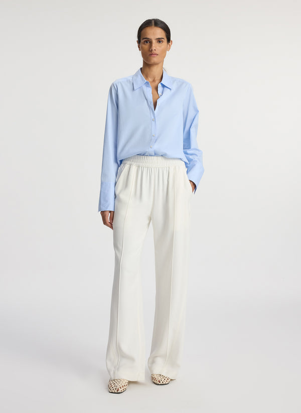 front view of woman wearing light blue button down collared shirt and white pants