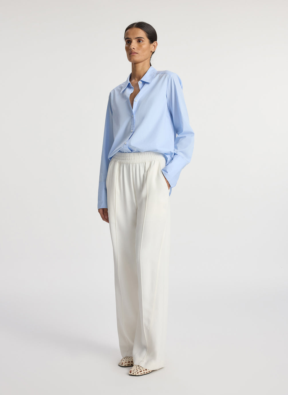side view of woman wearing light blue button down collared shirt and white pants
