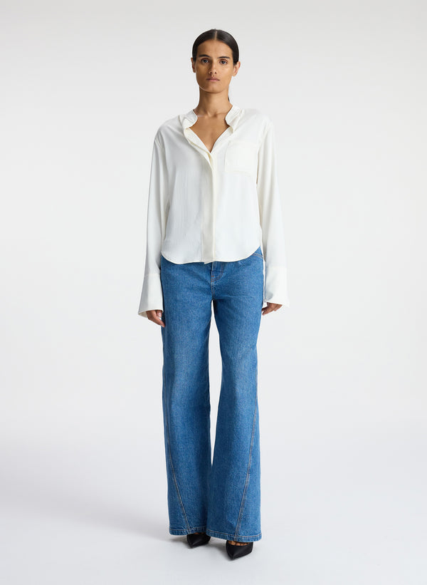 front view of woman wearing white satin long sleeve button down and medium blue wash denim jeans