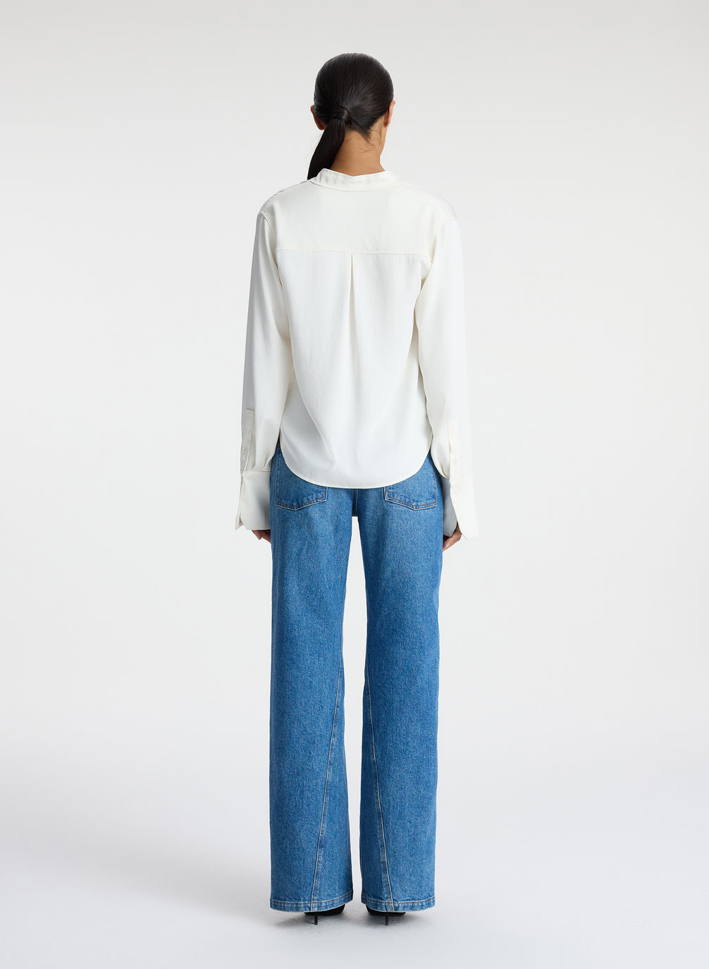 back view of woman wearing white satin long sleeve button down and medium blue wash denim jeans