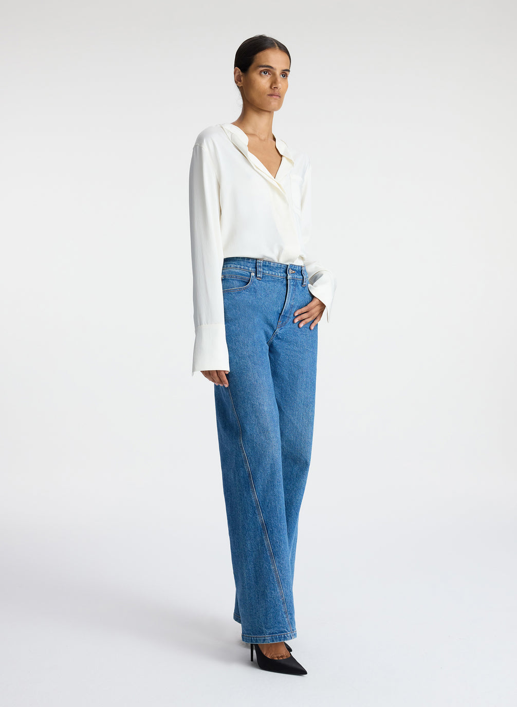 side view of woman wearing white satin long sleeve button down and medium blue wash denim jeans