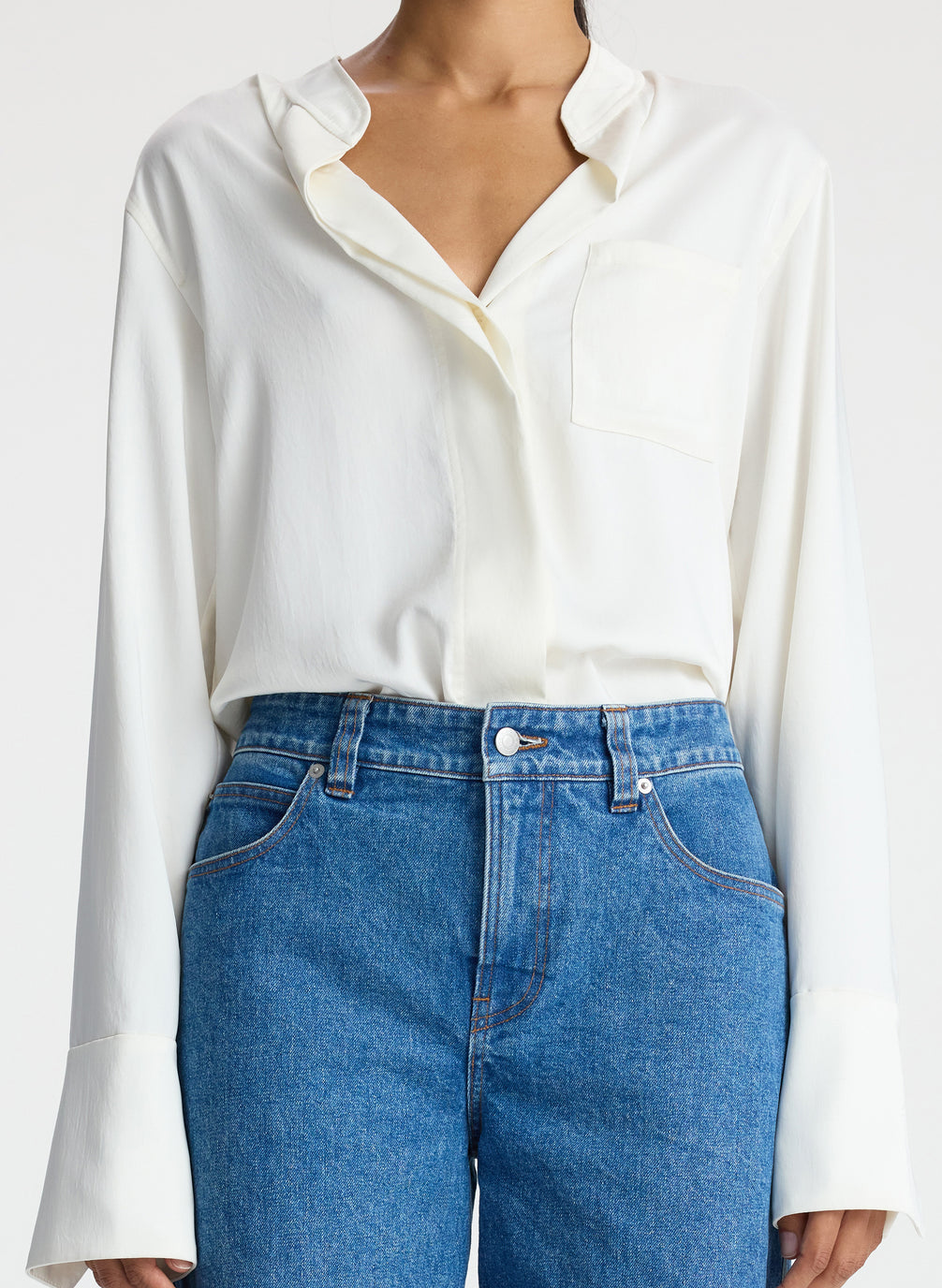 detail view of woman wearing white satin long sleeve button down and medium blue wash denim jeans
