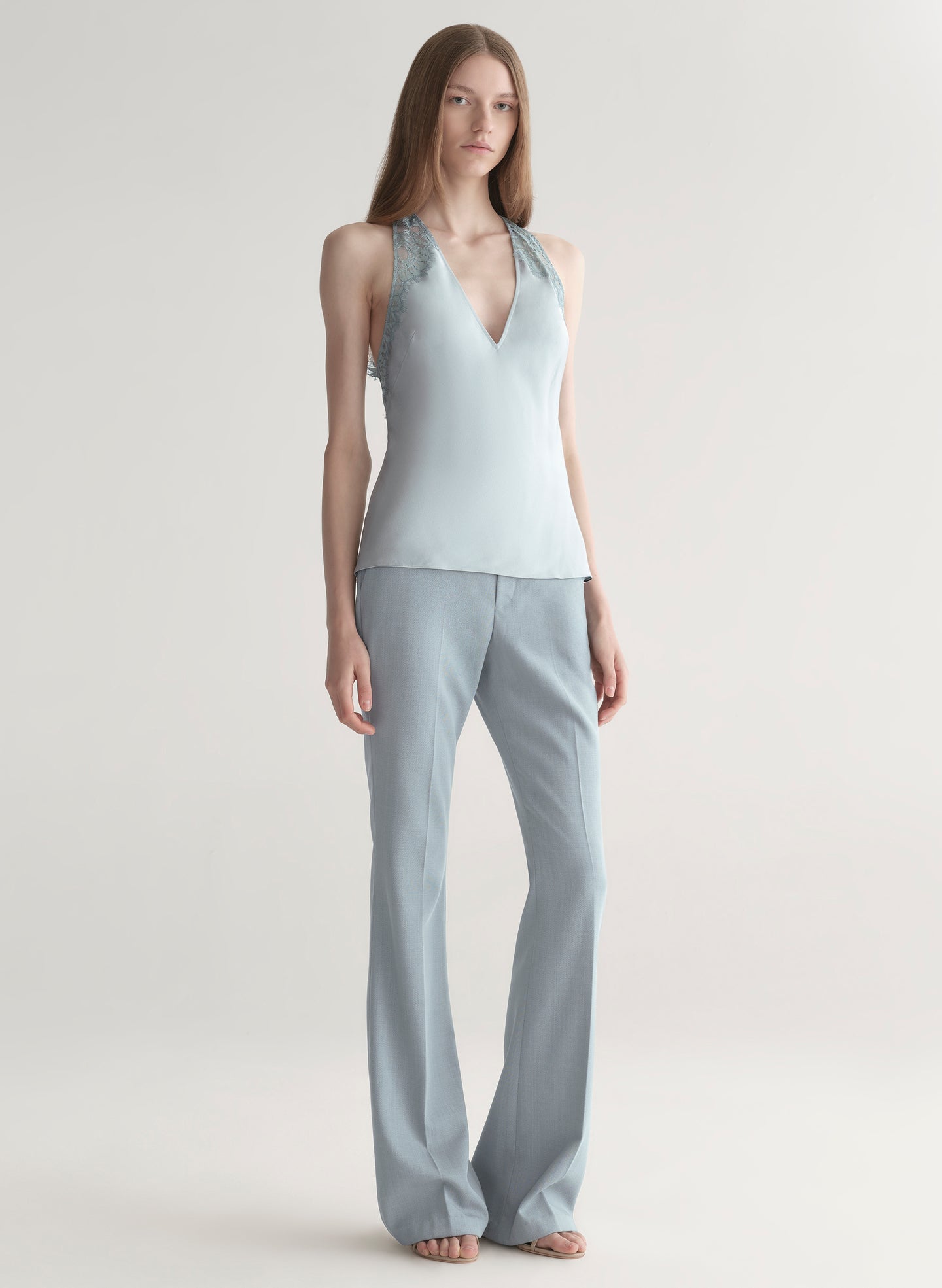 Woman wearing a light blue sleeveless top with lace details  and light blue pants on a plain background