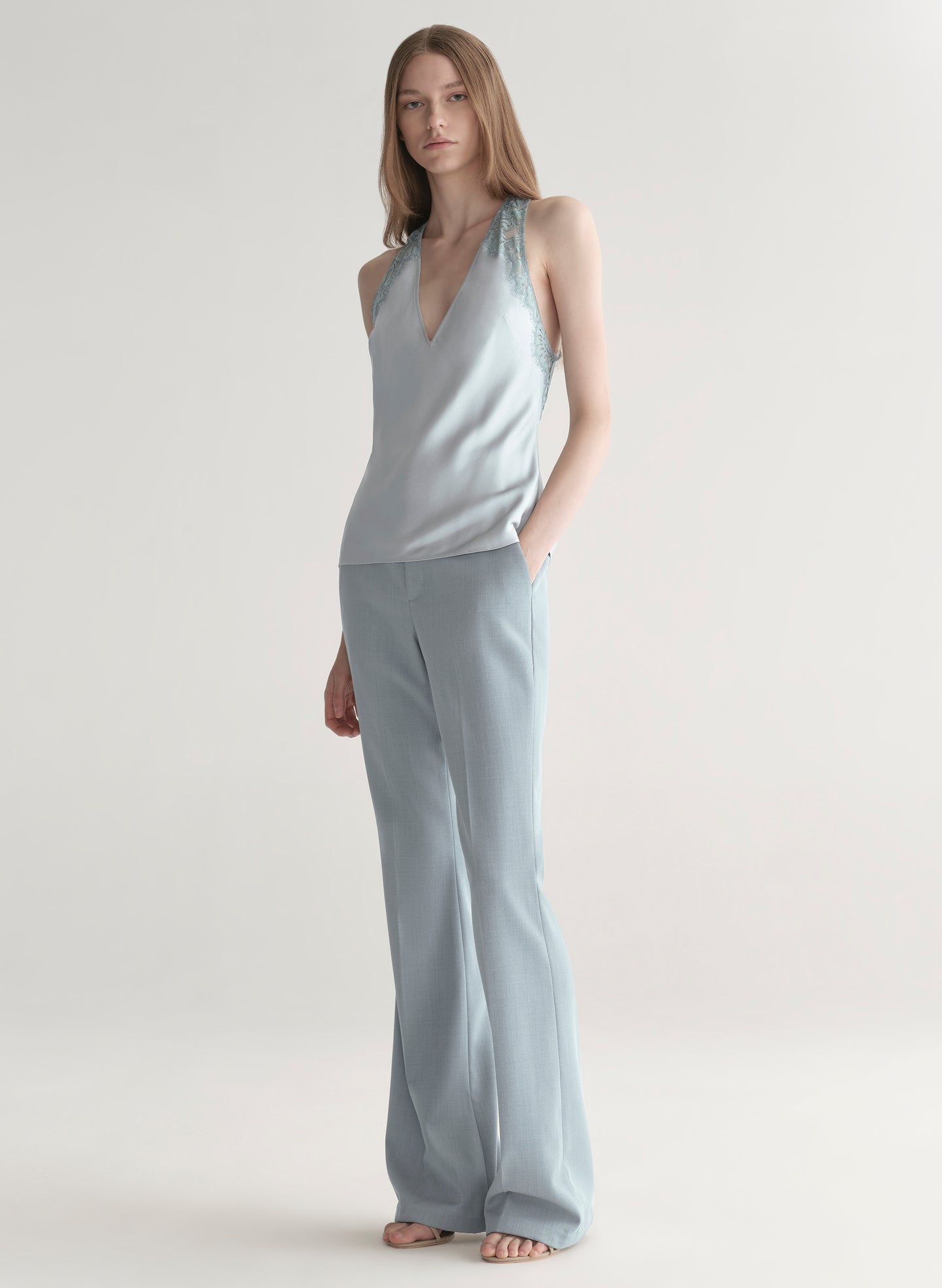 Woman wearing a light blue sleeveless top with lace details  and light blue pants on a plain background