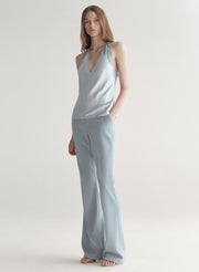 Woman wearing a light blue sleeveless top with lace details  and light blue pants on a plain background