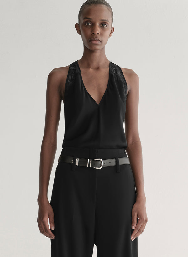 Person wearing a black sleeveless top and black pants with a belt on a plain background