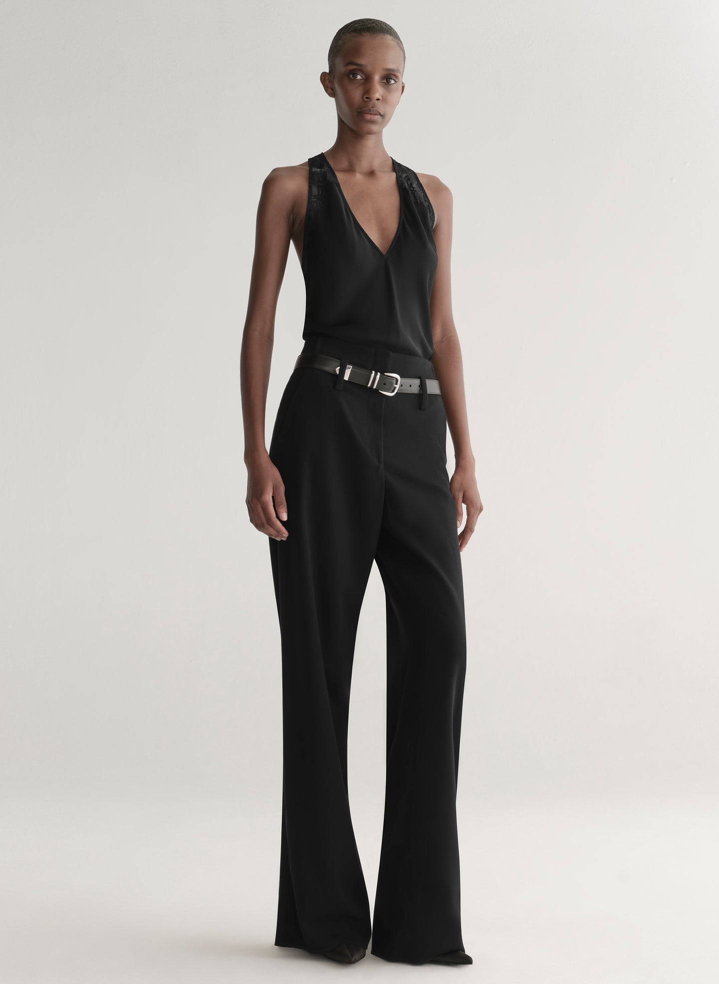 Person wearing a black sleeveless top and black pants with a belt on a plain background