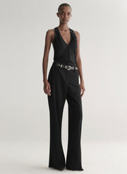 Person wearing a black sleeveless top and black pants with a belt on a plain background