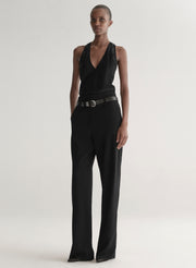 Person wearing a black sleeveless top and black pants with a belt on a plain background