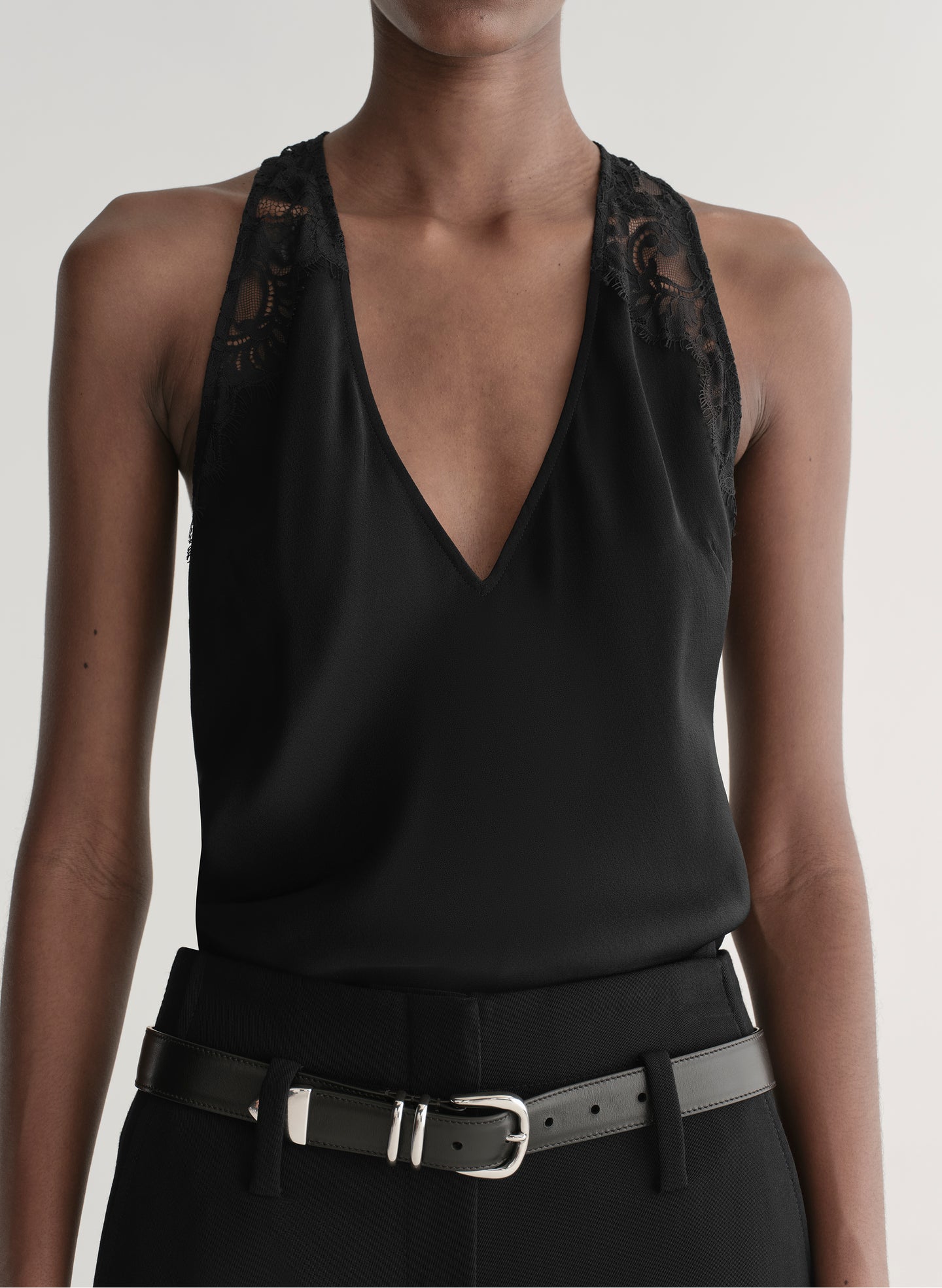 Person wearing a black sleeveless top and black pants with a belt on a plain background