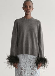 Woman wearing a grey sweater with feather details  and a lace skirt on a plain background