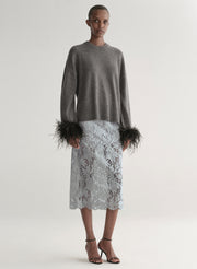 Woman wearing a grey sweater with feather details  and a lace skirt on a plain background