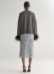 Woman wearing a grey sweater with feather details  and a lace skirt on a plain background