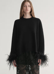 Woman wearing a black sweater with feather details  and a lace skirt on a plain background