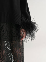 Woman wearing a black sweater with feather details  and a lace skirt on a plain background