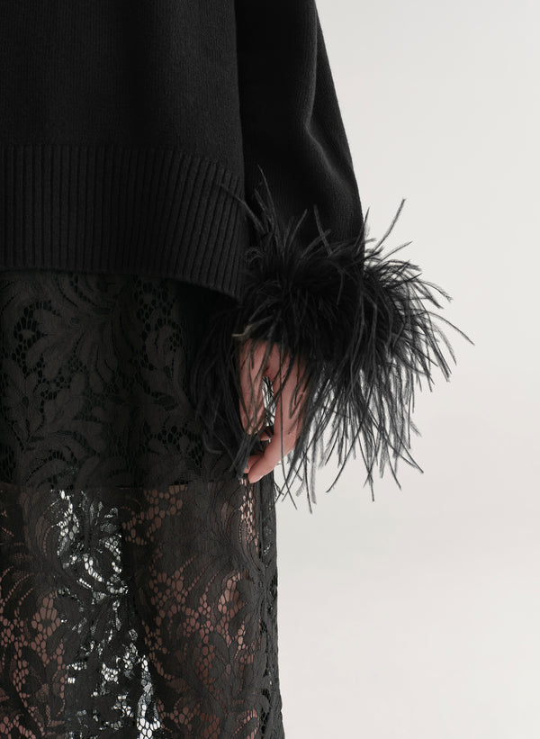 Woman wearing a black sweater with feather details  and a lace skirt on a plain background