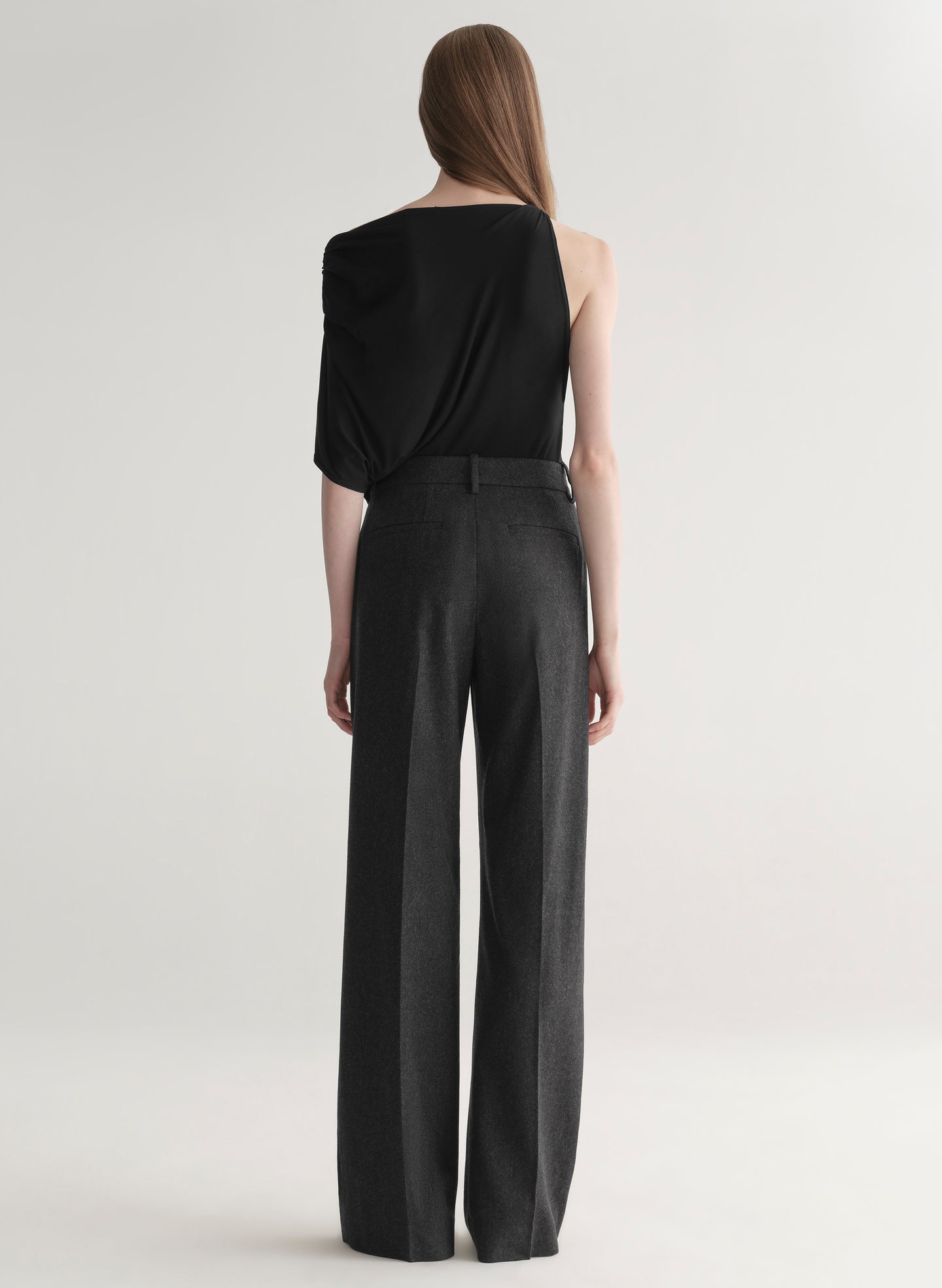 Woman wearing a black one-shoulder top and wide-leg pants on a white background