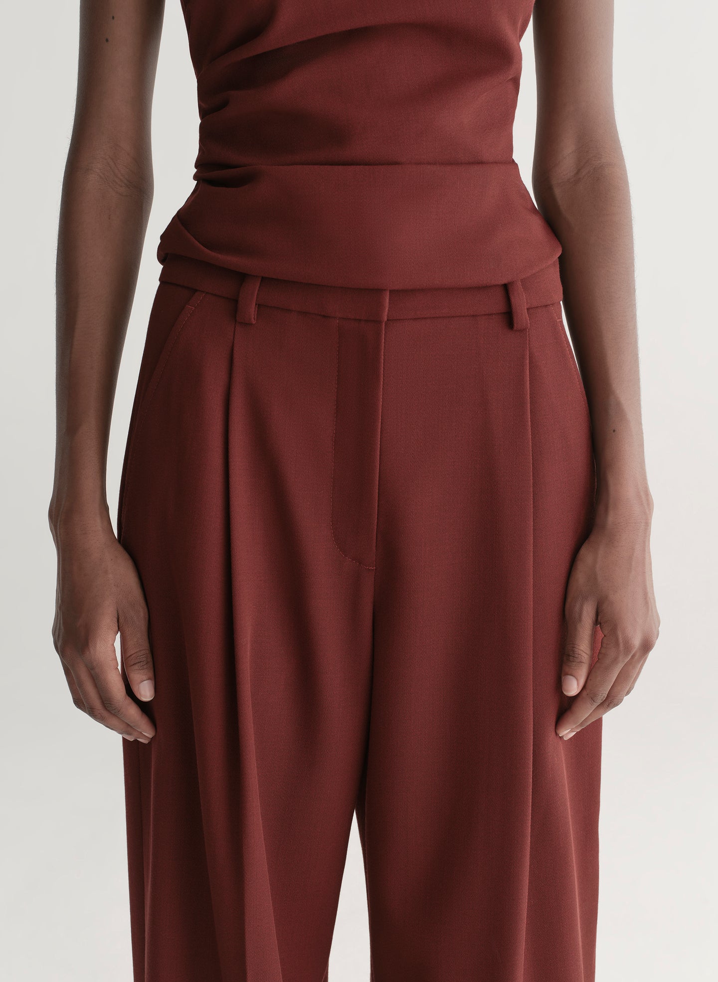 Person wearing a maroon one-shoulder top and wide-leg pants on a white background