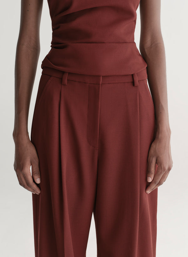 Person wearing a maroon one-shoulder top and wide-leg pants on a white background