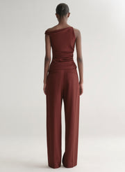 Person wearing a maroon one-shoulder top and wide-leg pants on a white background
