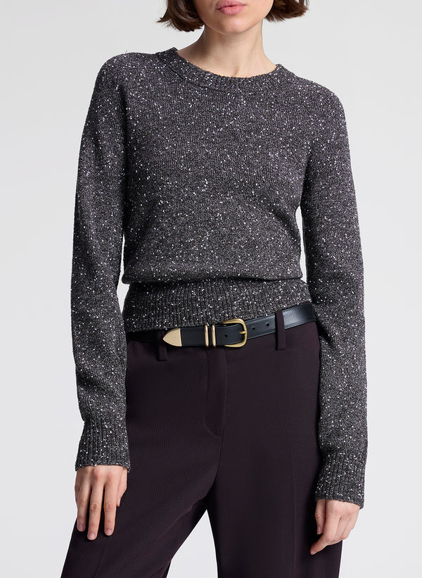 Woman wearing a gray speckled sweater and purple pants on a light gray background