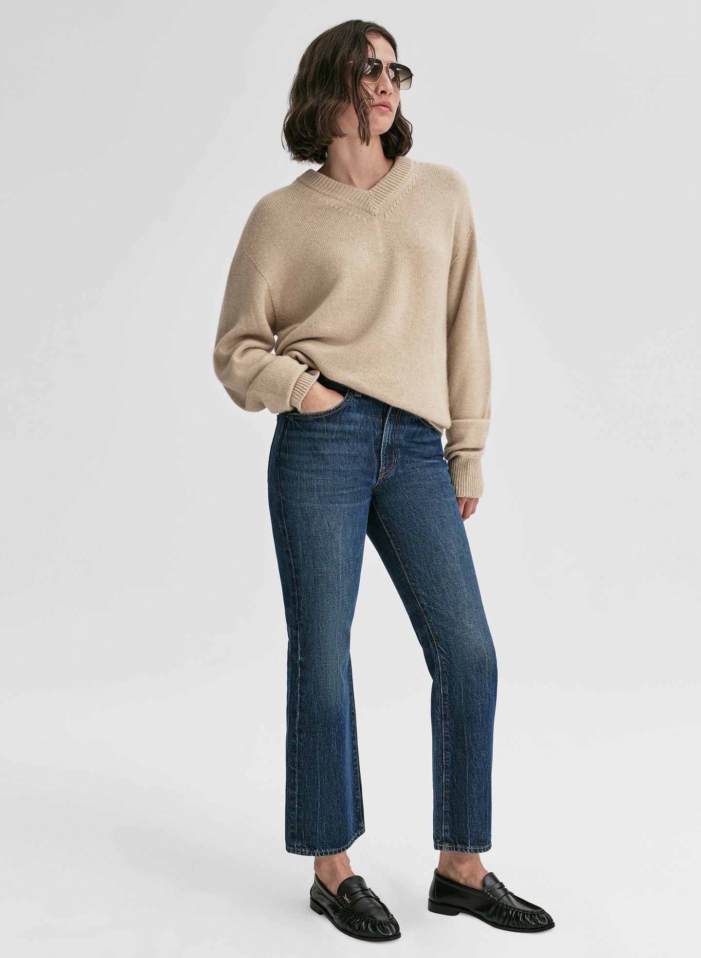 Person wearing a beige sweater and blue jeans on a white background