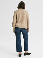 Person wearing a beige sweater and blue jeans on a white background