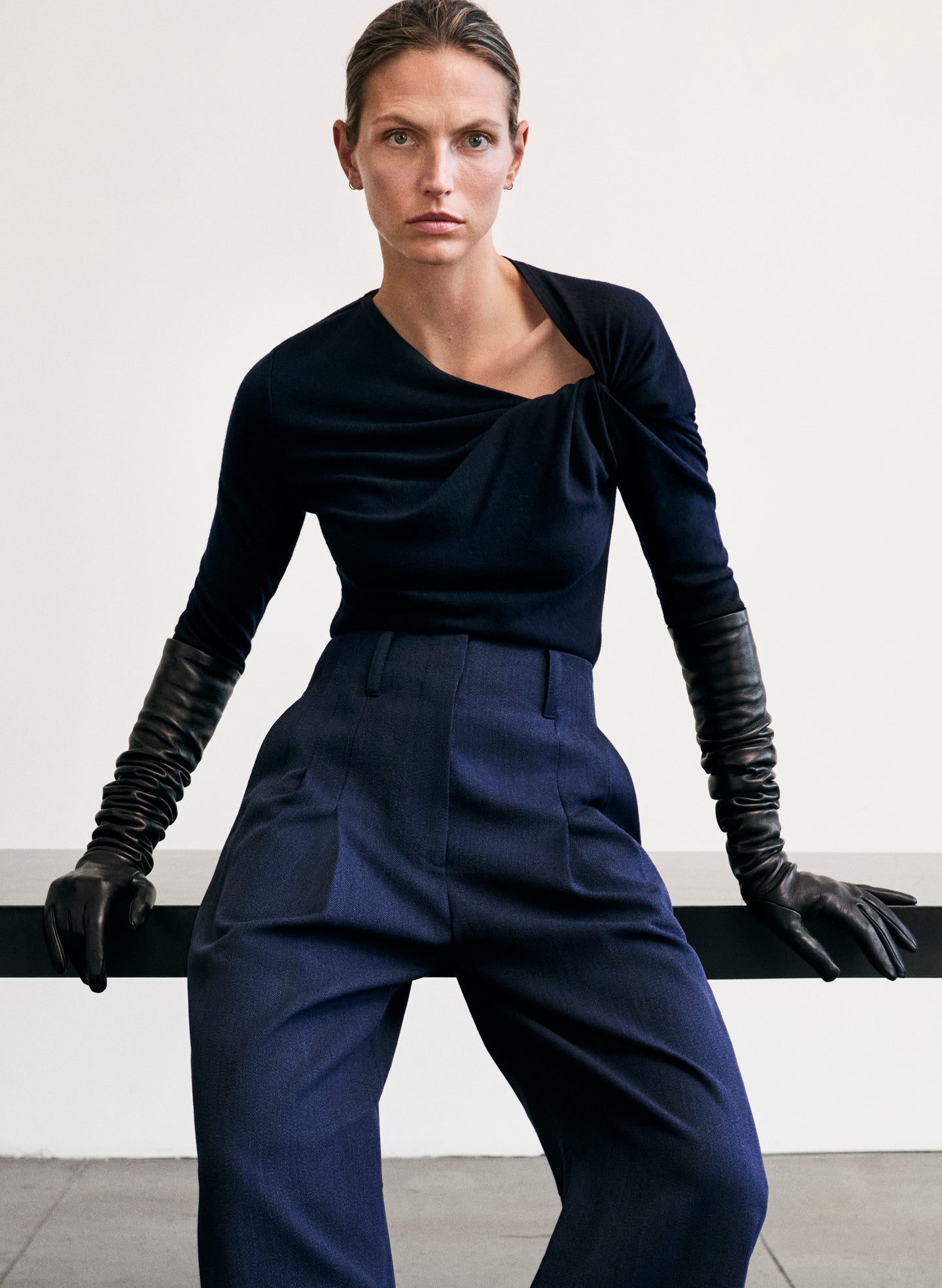 Woman wearing a dark blue outfit with gloves against a plain background