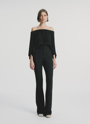 video view of woman wearing black satin pleated off the shoulder top with black pants