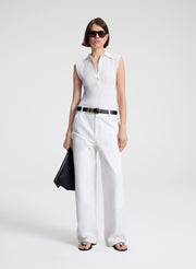 Woman wearing a white sleeveless top and pants with a black belt on a white background