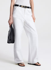 Person wearing white pants with a belt and holding a black clutch against a white background