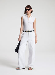 Woman wearing a white sleeveless shirt and white pants with a black belt on a white background