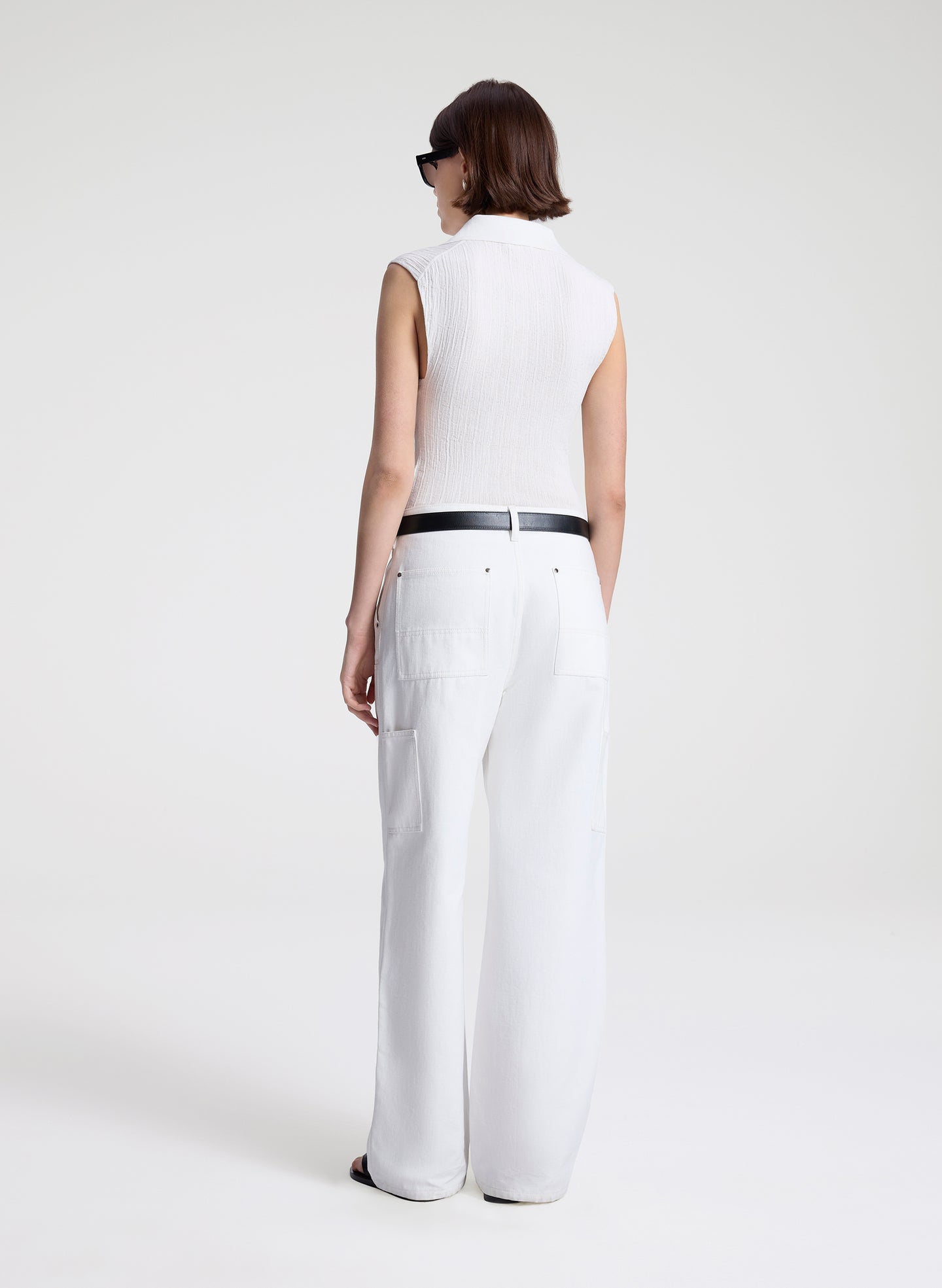 Person wearing a white sleeveless top and wide-leg pants on a plain background