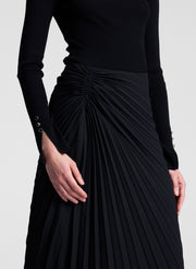 Black pleated skirt worn with a black long-sleeve top on a light gray background