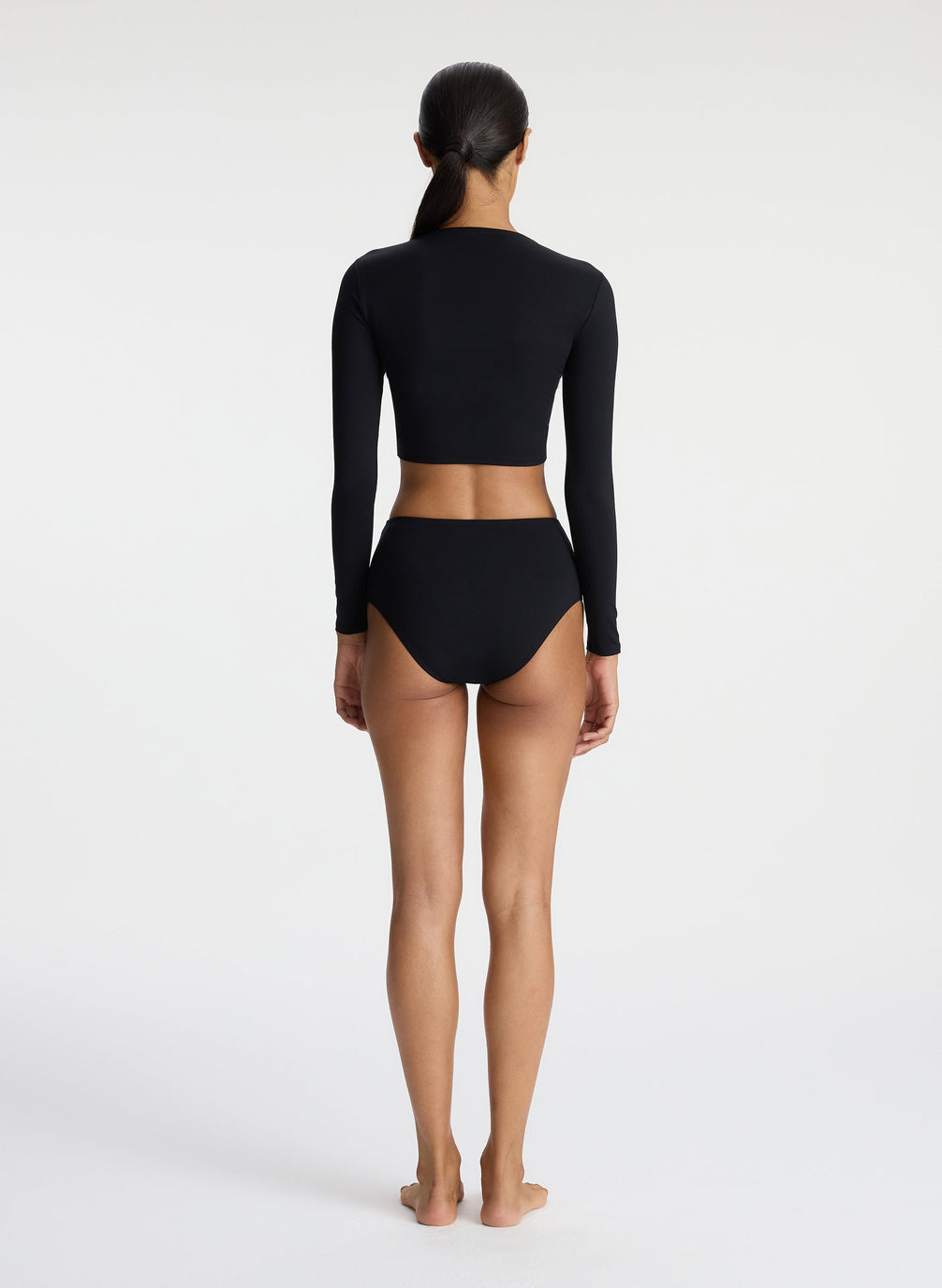 back view of woman in black long sleeve ruched rashguard and black bikini bottom