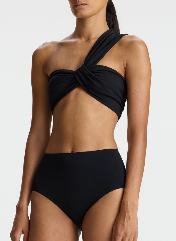 detail view of woman wearing black one shoulder swimsuit top and bikini bottom