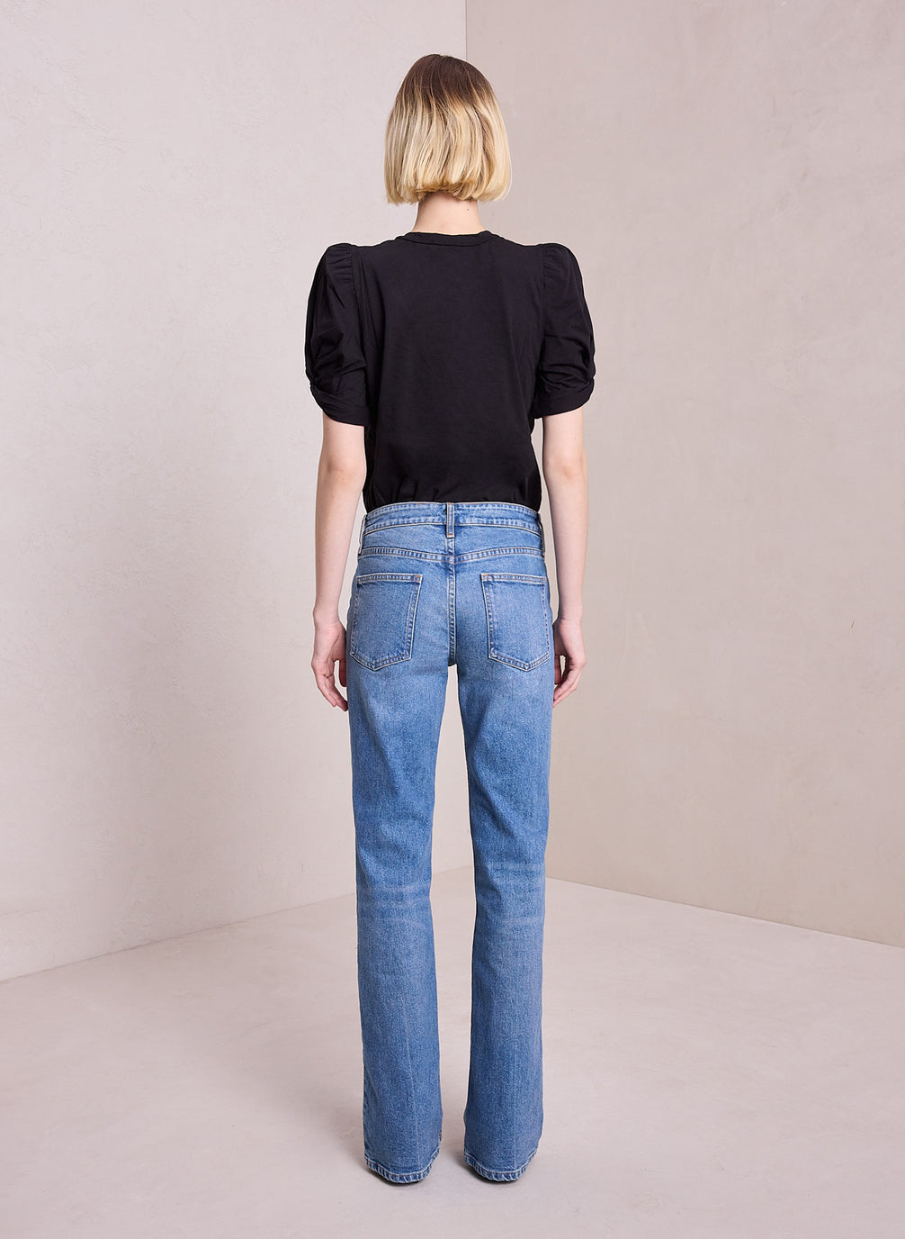 back view of woman wearing black puff sleeve tshirt and light blue wash denim jeans